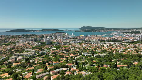 Paisaje-Urbano-De-Toulon-Con-Exuberante-Vegetación,-Mar-Azul-Y-Cielo-Despejado,-Vista-Aérea