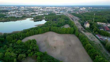 Panorama,-drone-view-of-the-lake,-forest,-field,-and-industrial-district-buildings-of-the-city