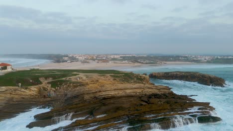 Zona-Residencial-Del-Pueblo-Baleal-En-La-Cima-De-Una-Colina,-Toma-Aérea-De-Seguimiento-Hacia-Las-Olas-Rompiendo-En-La-Costa-Rocosa