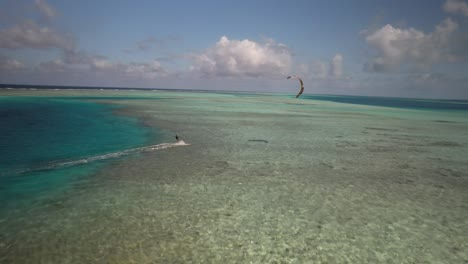 Kitesurfer-gliding-over-clear-turquoise-waters,-drone-following,-sunny-day,-tropical-vibe,-aerial-view