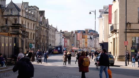 People-wandering-the-busy-cobbled-streets-of-Oxford-City,-lined-with-colourful-buildings,-retail-shops,-and-businesses-in-England-UK