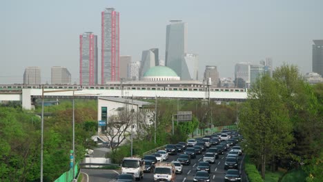 Trains-Travel-on-Dangsan-Railway-Bridge,-Cars-Traffic-Jam-on-Olympic-daero-Road,-National-Assembly-of-Korea-and-Yeouido-Financial-District-Skyscrapers-in-Background