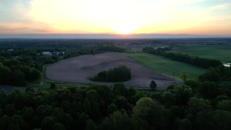 Panorama-Al-Atardecer,-Vista-De-Un-Paisaje-Con-Un-Bosque,-Campos-Y-El-Sol-Poniente