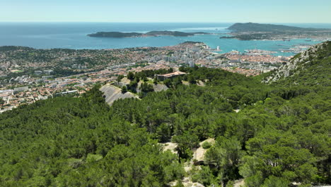 Toulon-and-fort-faron-surrounded-by-lush-green-forest-and-the-mediterranean-sea,-aerial-view