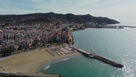 Vista-Aérea-Panorámica-De-La-Costa-De-Sitges-Y-Edificios-Históricos-Bajo-Un-Cielo-Soleado