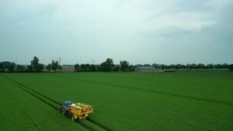 Tractor-with-folded-field-sprayer-drives-through-a-still-green-grain-field