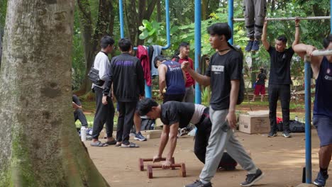 Hombre-Practicando-Calistenia-En-El-Parque-Taman-Kota-1,-BSD,-Indonesia,-Rodeado-De-Otros-En-Equipo-De-Entrenamiento.