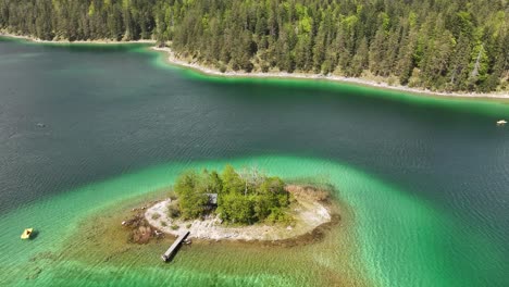 Vista-Aérea-De-Una-Pequeña-Y-Exuberante-Isla-Verde-Con-Un-Muelle-De-Madera,-Rodeada-Por-Las-Aguas-Cristalinas-Y-Turquesas-Del-Lago-Seerenbachfälle,-Ubicado-En-Amden-Betlis,-Walensee,-Suiza