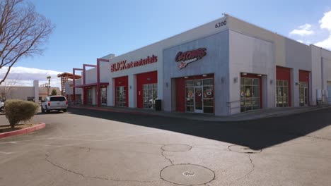 Vista-Soleada-De-Un-Centro-Comercial-Con-Artículos-De-Arte-Y-Tiendas-De-Electrónica,-Que-Muestra-Una-Arquitectura-Comercial-Moderna-Y-Un-Amplio-Estacionamiento.