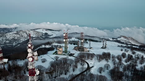 Snowy-mountain-landscape-with-radio-towers-and-a-church,-surrounded-by-bare-winter-trees