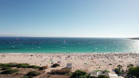 Acérquese-A-La-Vista-Aérea-De-Kitesurfistas-Practicando-Y-Divirtiéndose-En-La-Playa-De-Tarifa,-Cádiz,-España.