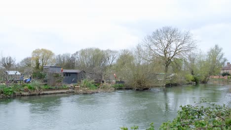 Scenic-pan-of-the-River-Thames-with-local-community-allotment-gardens-and-traditional-red-brick-houses-overlooking-the-river-in-Oxford-City,-England-UK