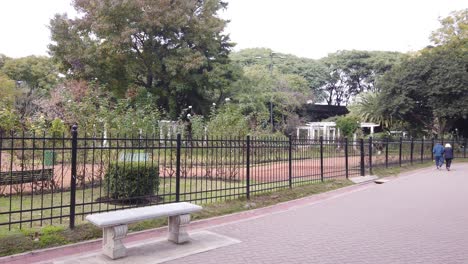 Zwei-ältere-Menschen,-Ein-Paar-Geht-Händchen-Haltend-Durch-Einen-Grünen,-Herbstlichen-Stadtpark-Mit-Panoramablick