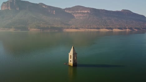 A-sunken-church-tower-in-the-tranquil-waters-of-Pantano-de-Sau,-surrounded-by-mountains