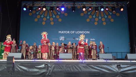 Bailarines-Indonesios-Vestidos-Con-Trajes-Rojos-Tradicionales-Y-Tocados-Dorados-Bailan-En-El-Escenario-Con-Abanicos-Rojos-Mientras-Otros-Tocan-La-Batería-En-Trafalgar-Square,-El-Festival-Anual-Eid-Del-Alcalde-De-Londres.