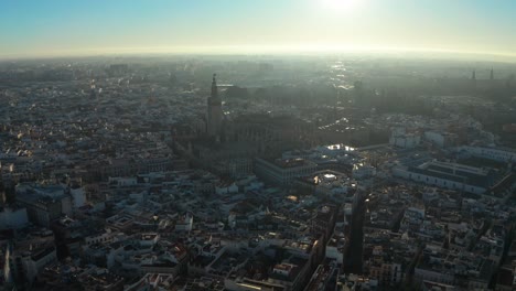 Luftaufnahme-Einer-Drohne-über-Sevilla,-Flug-In-Richtung-Der-Kathedrale-Mit-Hoch-Am-Himmel-Stehender-Sonne