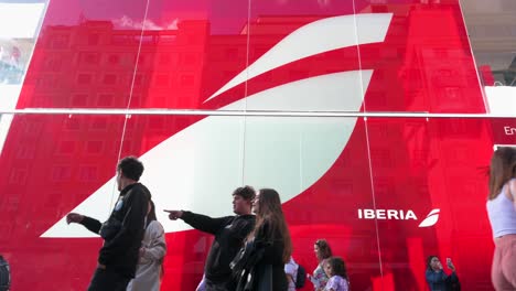 Low-angle-view-of-pedestrians-walking-past-the-Spanish-airline-Iberia's-pop-up-store-on-the-retail-and-entertainment-street-of-Gran-Via-in-Madrid,-Spain