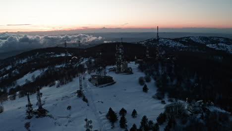 Schneebedeckter-Berg-Mit-Kommunikationstürmen-Im-Morgengrauen,-Mit-Einer-Ruhigen-Winterlandschaft