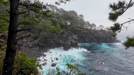 Dramatische-Küstenlinie-Bei-Schlechtem-Wetter,-Die-Das-Wasser-Zeigt,-Das-Auf-Die-Klippen-Stürzt,-Die-Vom-Wald-In-Japan-Aus-Zu-Sehen-Sind