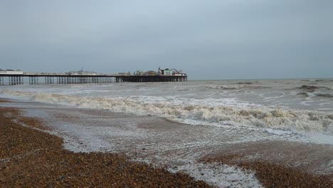 Blick-Auf-Den-Pier-Von-Brighton-An-Einem-Bewölkten-Tag-Mit-Wellen,-Die-In-Zeitlupe-Brechen