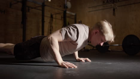 Blond-male-doing-push-up-repetitions-on-gym-floor,-side-view