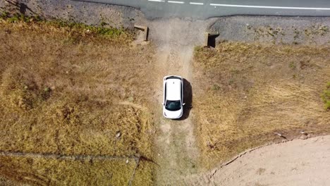 A-white-car-driving-on-a-rural-dirt-road-in-dry-fields-of-cordoba,-spain,-aerial-view