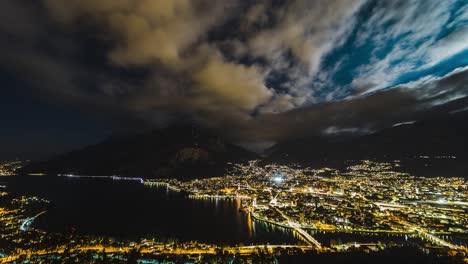 Lapso-Nocturno-De-La-Ciudad-Italiana-De-Lecco-Al-Pie-De-Las-Montañas-Con-Nubes-Y-Luces-De-La-Ciudad.