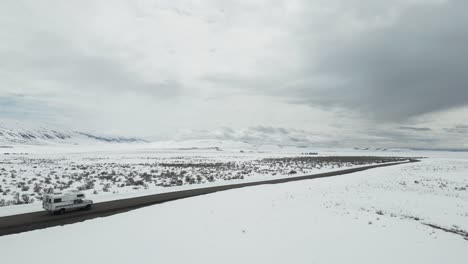 Aerial-view-of-a-white-camper-van-journeying-through-Idaho's-snowy,-barren-landscape
