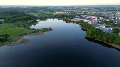 Panorama-at-sunrise,-drone-view-of-industrial-district-buildings-of-the-city-located-beyond-the-shores-of-the-lake