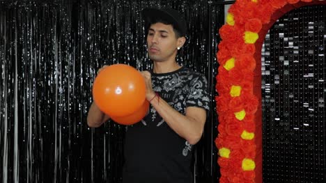 Latino-man-tying-together-orange-balloons-for-Día-de-muertos-party