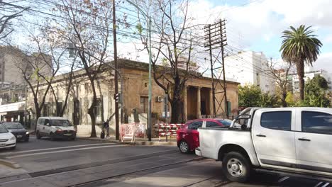 Modern-cars-cross-an-old-train-station-with-colonial-house-in-buenos-aires-city-argentina-panoramic-autumnal-day-with-local-greenery-at-flores-neighborhood