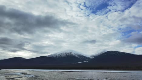 Timelapse-view-of-snow-covered-mountains-and-a-partially-frozen-river-under-a-cloudy-sky