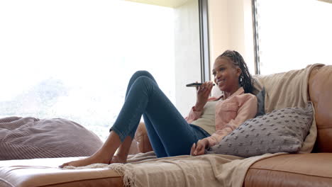African-American-young-woman-relaxing-on-sofa,-speaking-on-smartphone