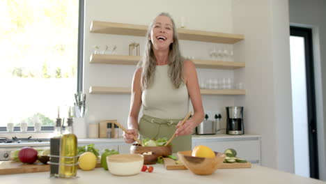 Caucasian-woman-preparing-salad-in-kitchen,-laughing