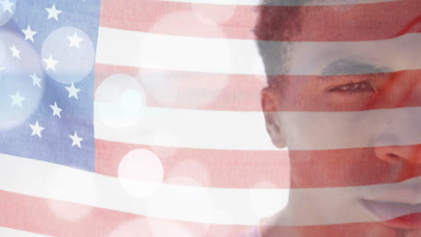 Animation-of-american-flag-and-light-spots-over-half-portrait-of-happy-biracial-man-on-sunny-beach