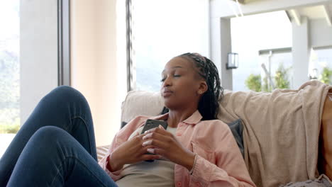 African-American-young-woman-relaxing-on-couch,-holding-smartphone