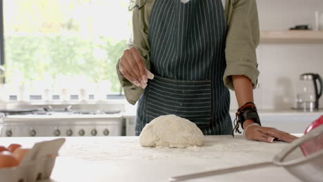 African-American-young-woman-wearing-apron,-making-dough-in-kitchen