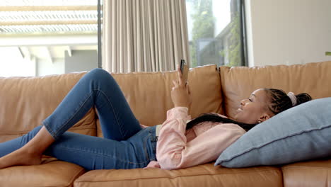 African-American-young-woman-lying-on-couch,-holding-smartphone