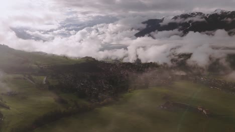 Foggy-mountain-landscape-with-low-clouds-drifting-over-green-fields-during-sunrise,-aerial-view