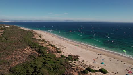 traveling-aerial-view-of-kitesurfers-doing-practice-and-having-fun-at-Tarifa-Beach,-Cadiz,-spain