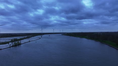 Fliegen-Sie-Bei-Sonnenuntergang-über-Den-Fluss-Mit-Windrädern-Im-Hintergrund-In-Der-Nähe-Von-Barendrecht,-Niederlande