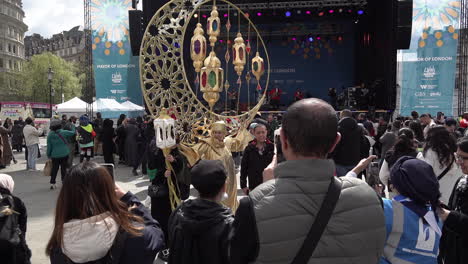 La-Gente-Toma-Fotografías-En-Sus-Teléfonos-Inteligentes-De-Una-Mujer-Con-Un-Traje-Ceremonial-Dorado-Con-Forma-De-Luna-Creciente-Gigante-Con-Linternas-En-Trafalgar-Square-En-El-Festival-Anual-Eid-Del-Alcalde-De-Londres.