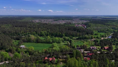 A-small-town-surrounded-by-vast-green-forest-and-blue-sky,-aerial-view