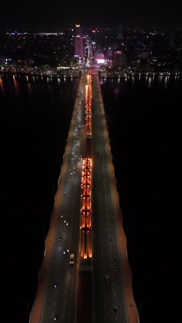 Aerial-night-view-looking-down-on-cars-driving-across-the-Da-Nang-Dragon-Bridge-in-Vietnam,-Saigon