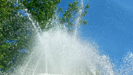 Water-fountain-in-close-up,-with-the-green-background-of-tree-leaves-and-the-blue-sky,-crystal-clear-water-makes-a-beautiful-effect