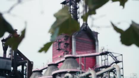 Steel-industry-plant-shot-with-tree-leafs-in-the-foreground,-focus-pull-to-background