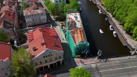 Building-construction-with-security-net-near-a-river-in-lithuania,-aerial-view