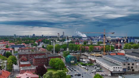 A-european-city-with-construction-cranes-under-a-cloudy-sky,-industrial-area,-aerial-view