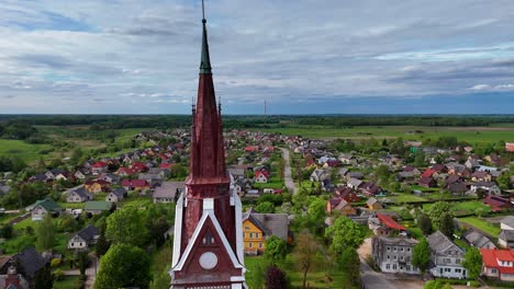 Sveksna-church-towers-and-village-in-lithuania,-surrounded-by-green-fields,-aerial-view