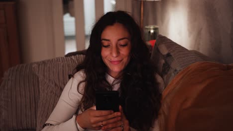 Young-Italian-woman-relaxes-on-the-sofa-while-scrolling-through-her-smart-phone